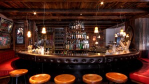 A bar area with a wooden ceiling, leather bar stools, and a variety of bottles and glasses on shelves.
