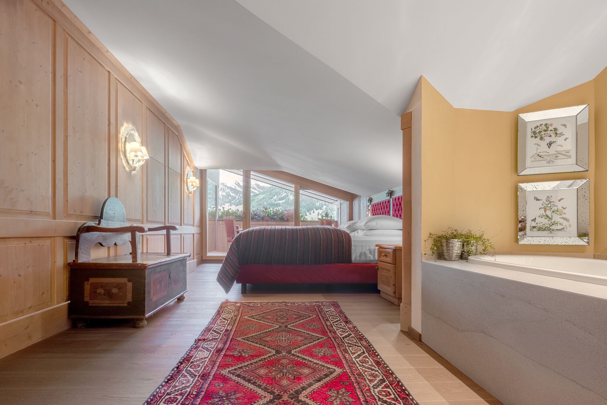 Ein Schlafzimmer mit einem großen Bett, einer Holzkommode, einem roten Teppich und einem Fenster mit Blick auf die Berge.