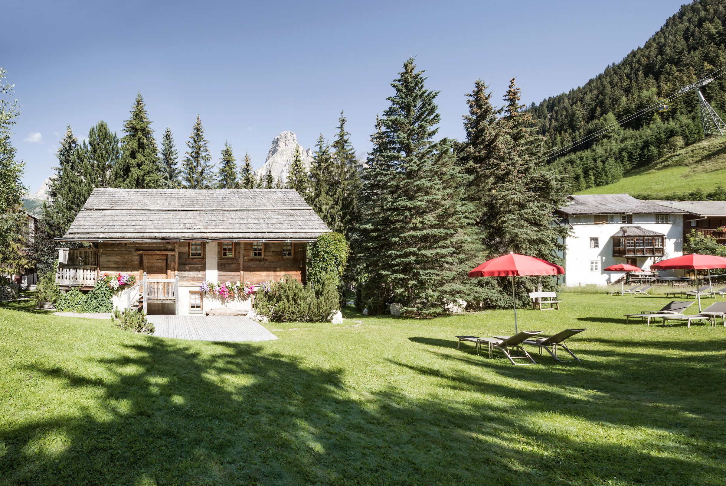 A lodge with a wooden exterior, surrounded by a well-maintained lawn and trees. There are outdoor seating areas with red umbrellas.