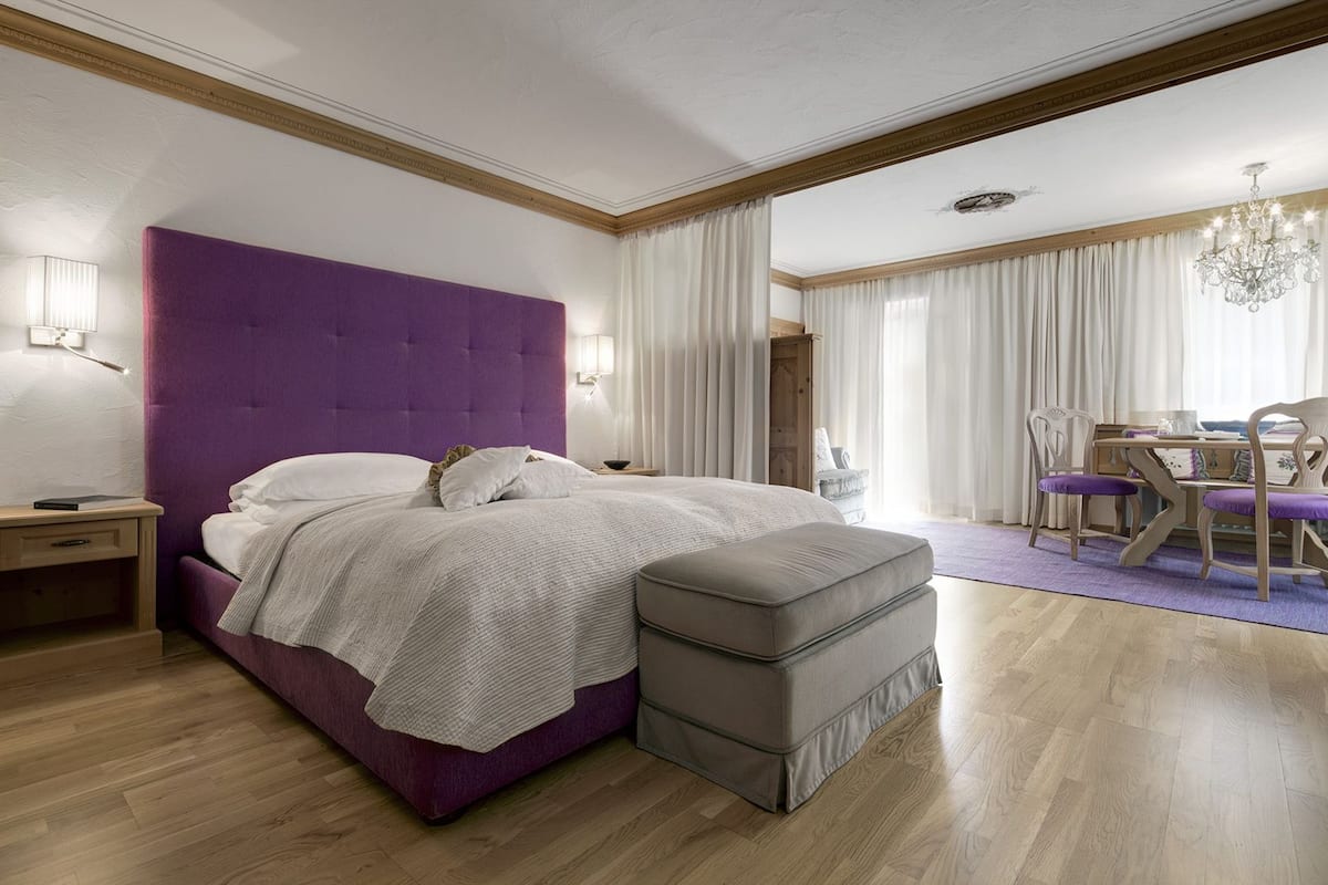 Een slaapkamer met een groot bed, een nachtkastje, een kaptafel, een bureau met stoelen en een kroonluchter.