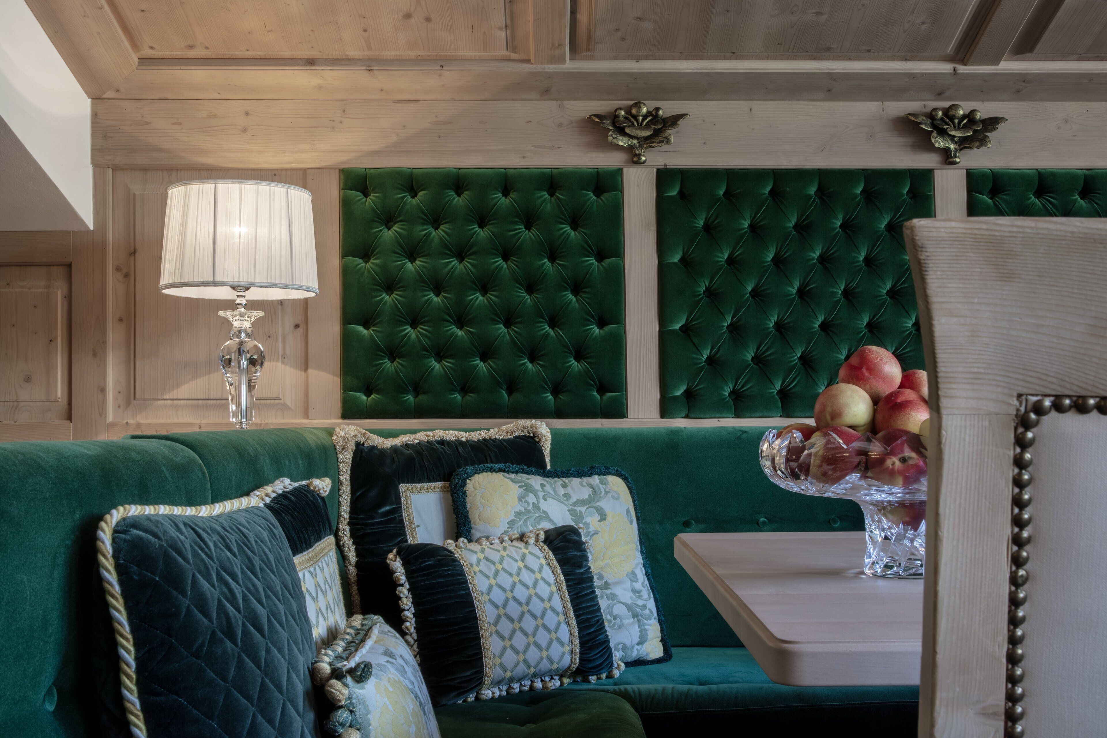 Un canapé vert recouvert de tissu, agrémenté de coussins décoratifs, une table sur laquelle est disposé un centre de table composé de fruits et une lampe.