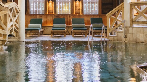An indoor swimming pool with wooden chairs and a wooden staircase.