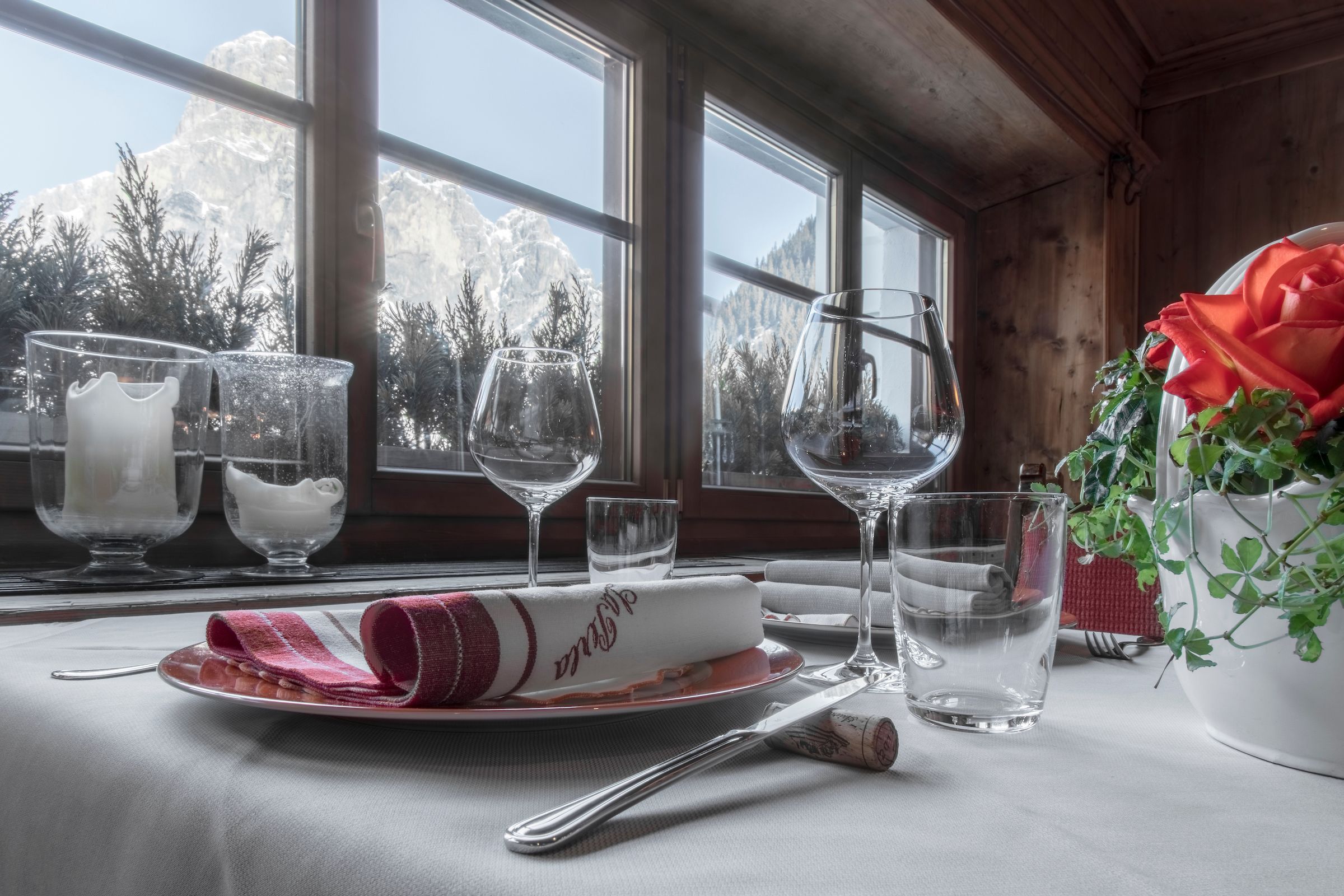 Una mesa de comedor con vasos, un plato con una servilleta y un florero con una rosa roja.