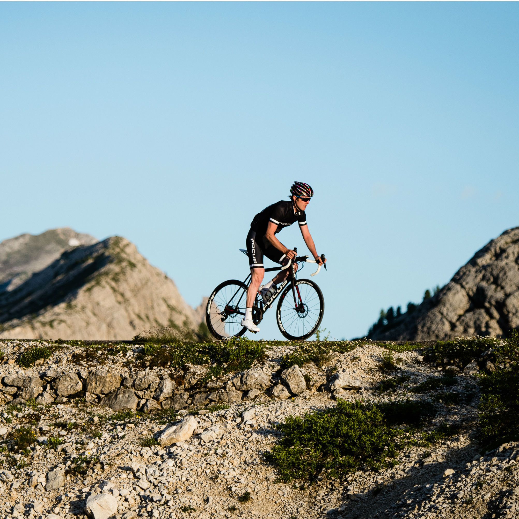 Un ciclista en un sendero de bicicleta de montaña con terreno rocoso y montañas al fondo.