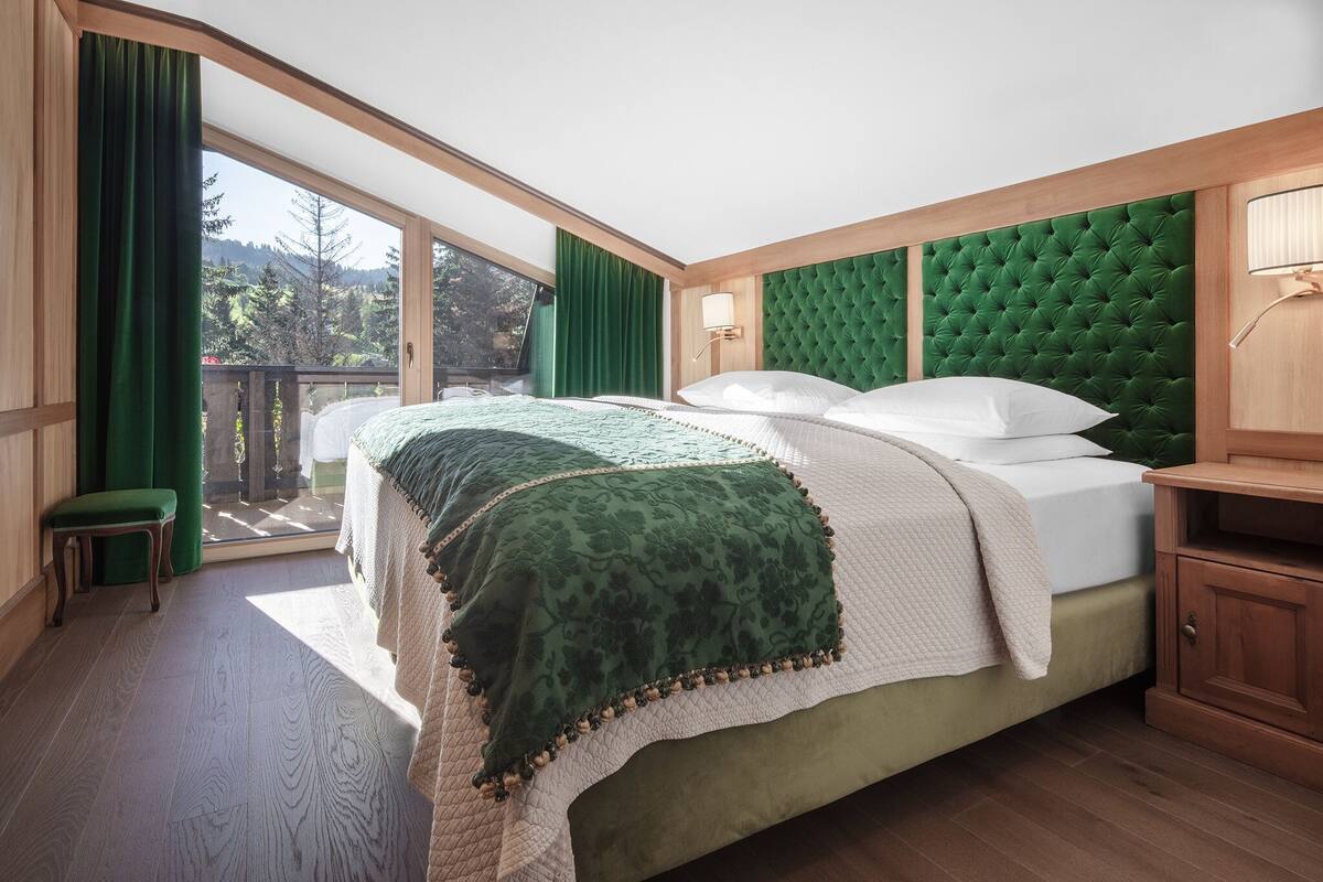 Een slaapkamer met een groot bed, groene gordijnen en uitzicht op bomen.