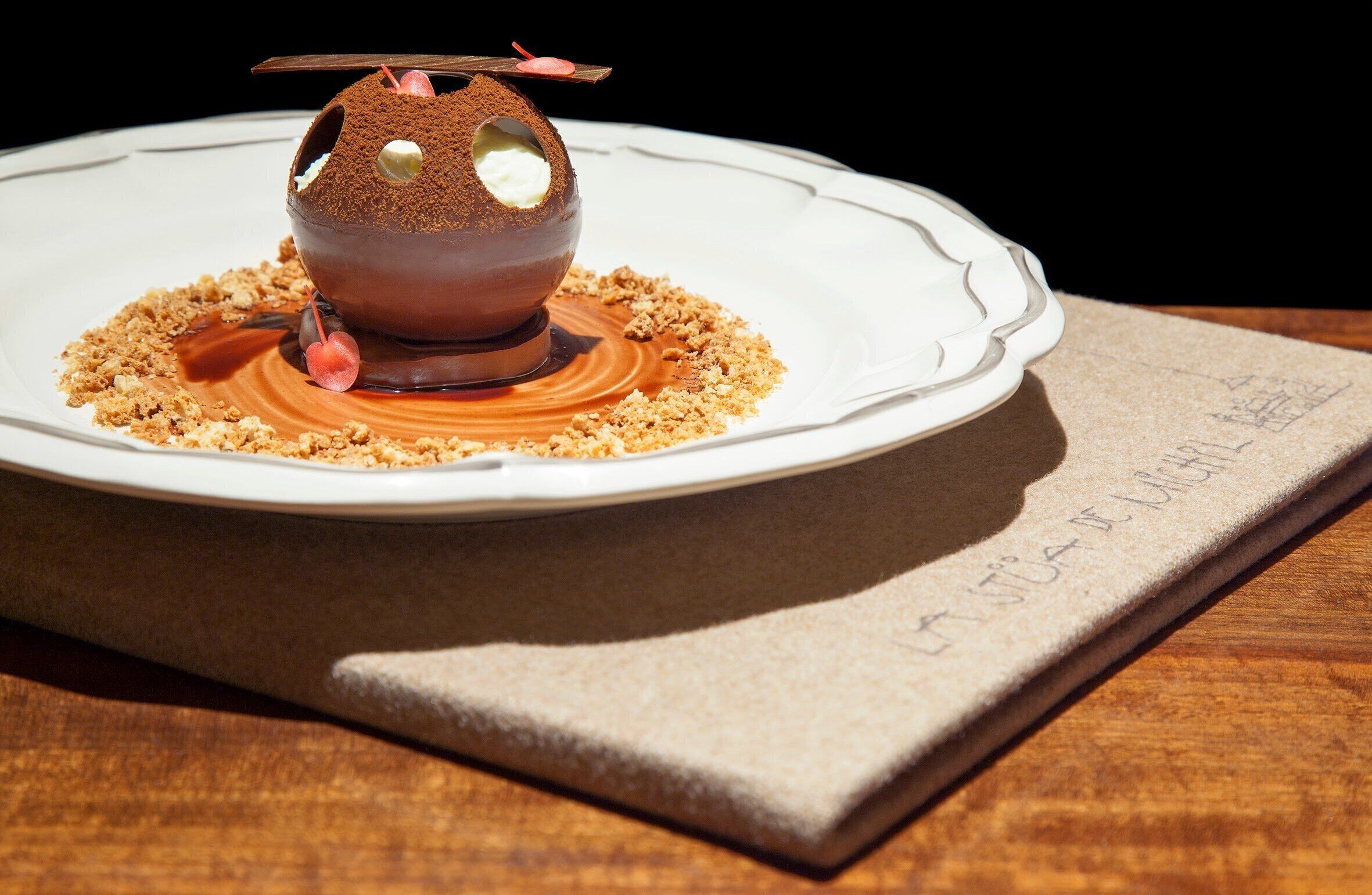 Ein Dessert auf einem weißen Teller mit zerbröselter Keksdecke, platziert auf einem Tisch mit Unterlage.