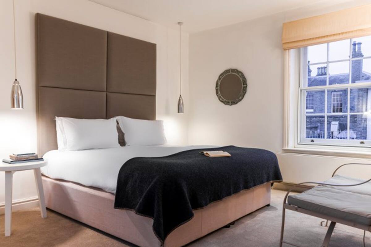 Une chambre à coucher avec un lit, une table de chevet et une fenêtre donnant sur des immeubles.