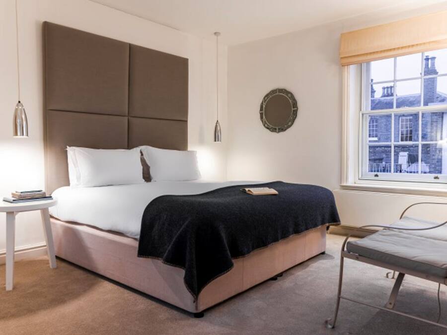 A bedroom with a bed, bedside table, and a window with a view of buildings.