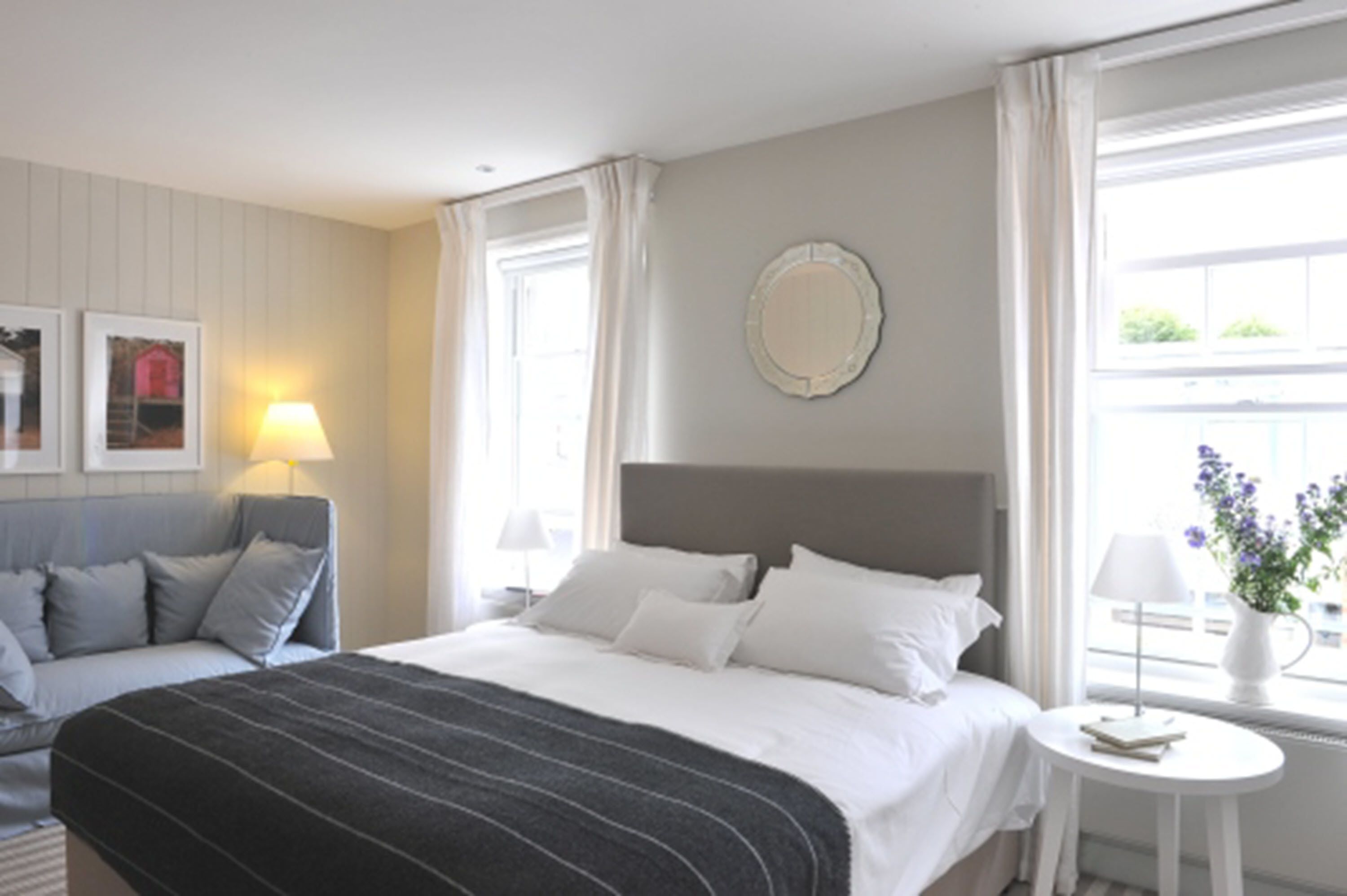 A hotel room with a bed, a sofa, a small table, a lamp, and a window with curtains.