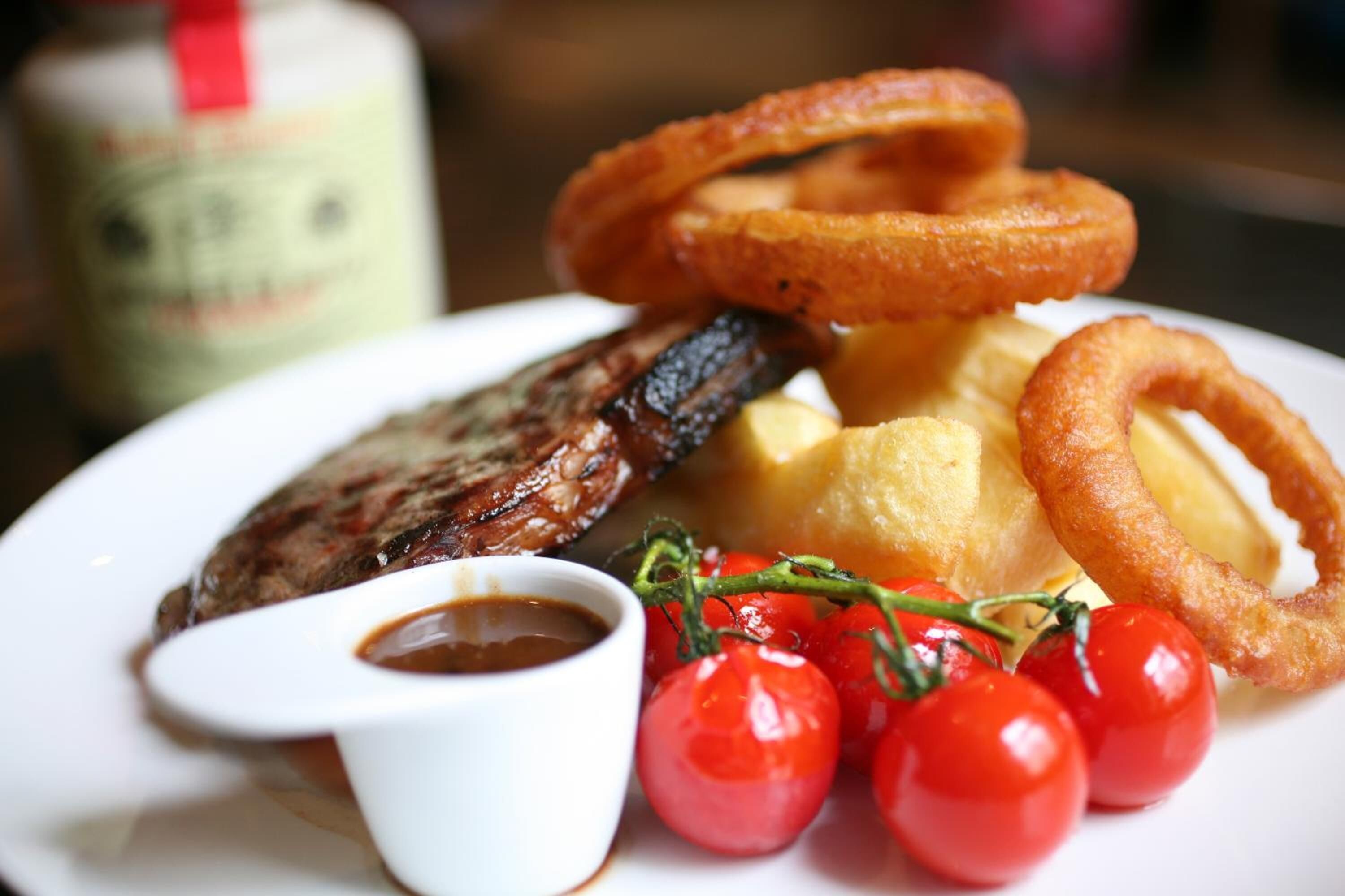 Ein Teller mit einem Steak, Yorkshire Pudding, Zwiebelringen, Cocktailtomaten und einer kleinen Soßenportion.