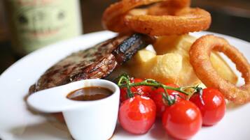 Ein Teller mit einem Steak, Yorkshire Pudding, Zwiebelringen, Cocktailtomaten und einer kleinen Soßenportion.