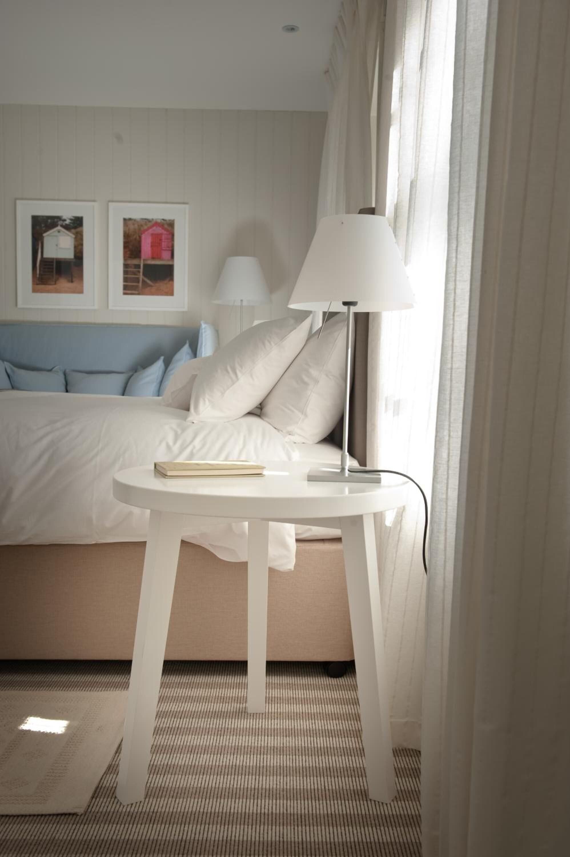 Habitación de hotel ordenada con una cama, una mesita de noche con lámpara y dos cuadros en la pared.