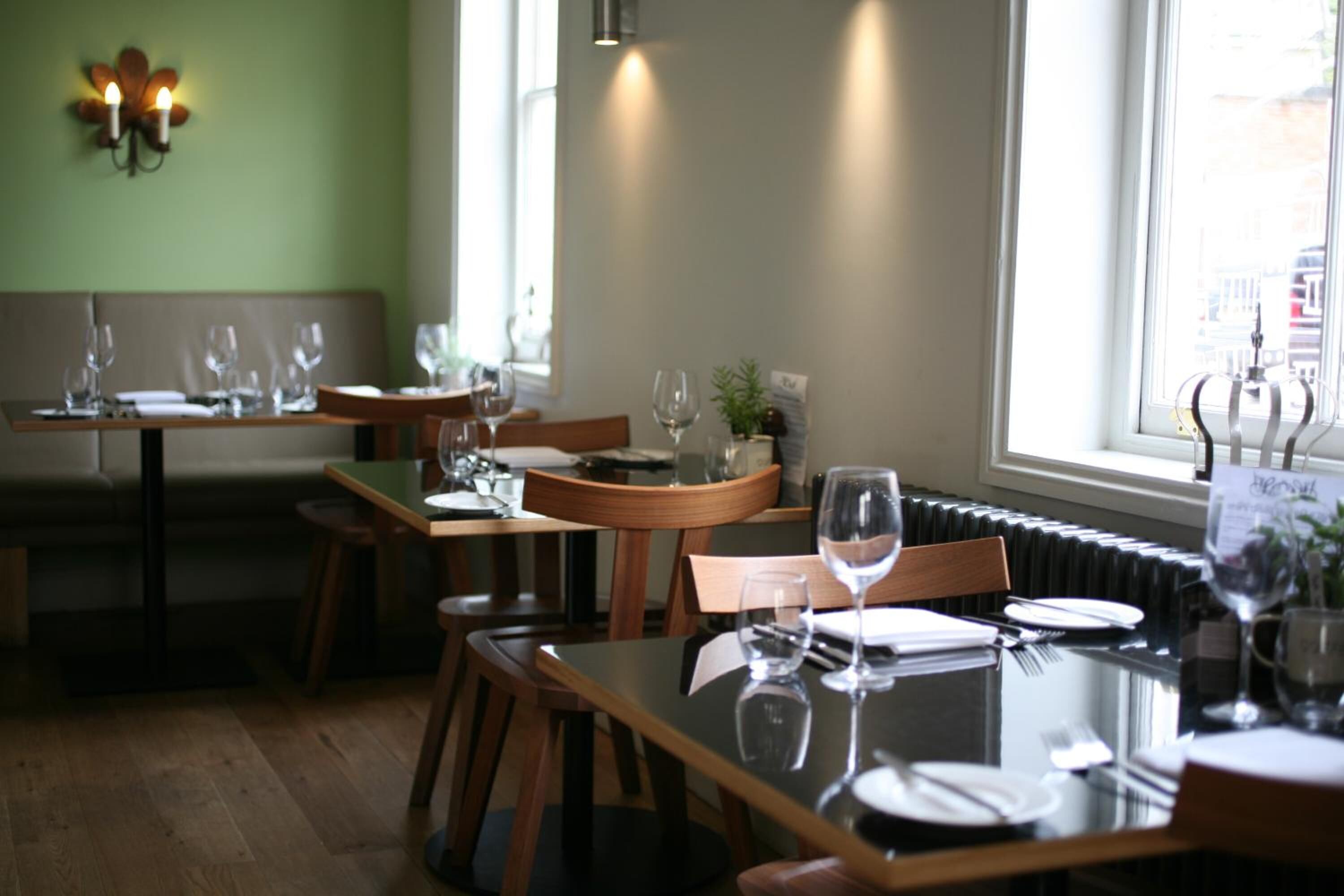 A restaurant with wooden tables and chairs, a green wall, and a window with a view of the city.