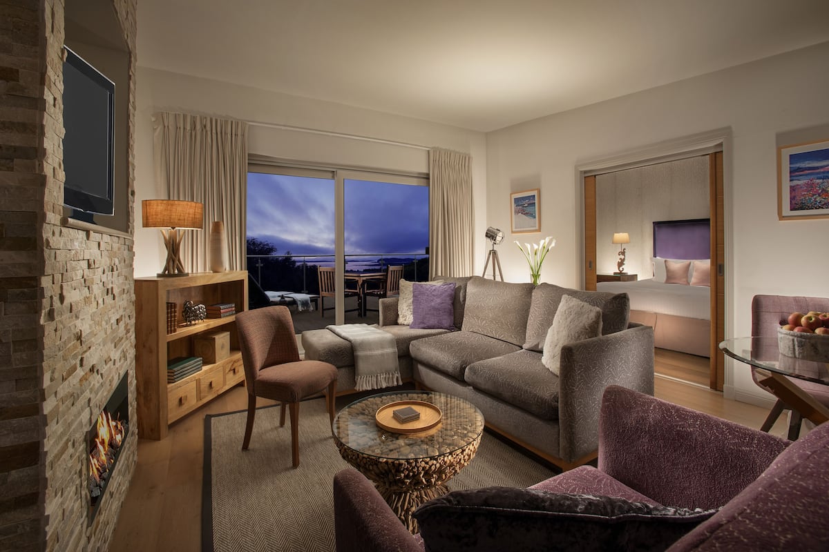 A modern living room with a fireplace, comfortable seating, a glass coffee table, and a view of the city at dusk.