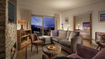 A modern living room with a fireplace, comfortable seating, a glass coffee table, and a view of the city at dusk.