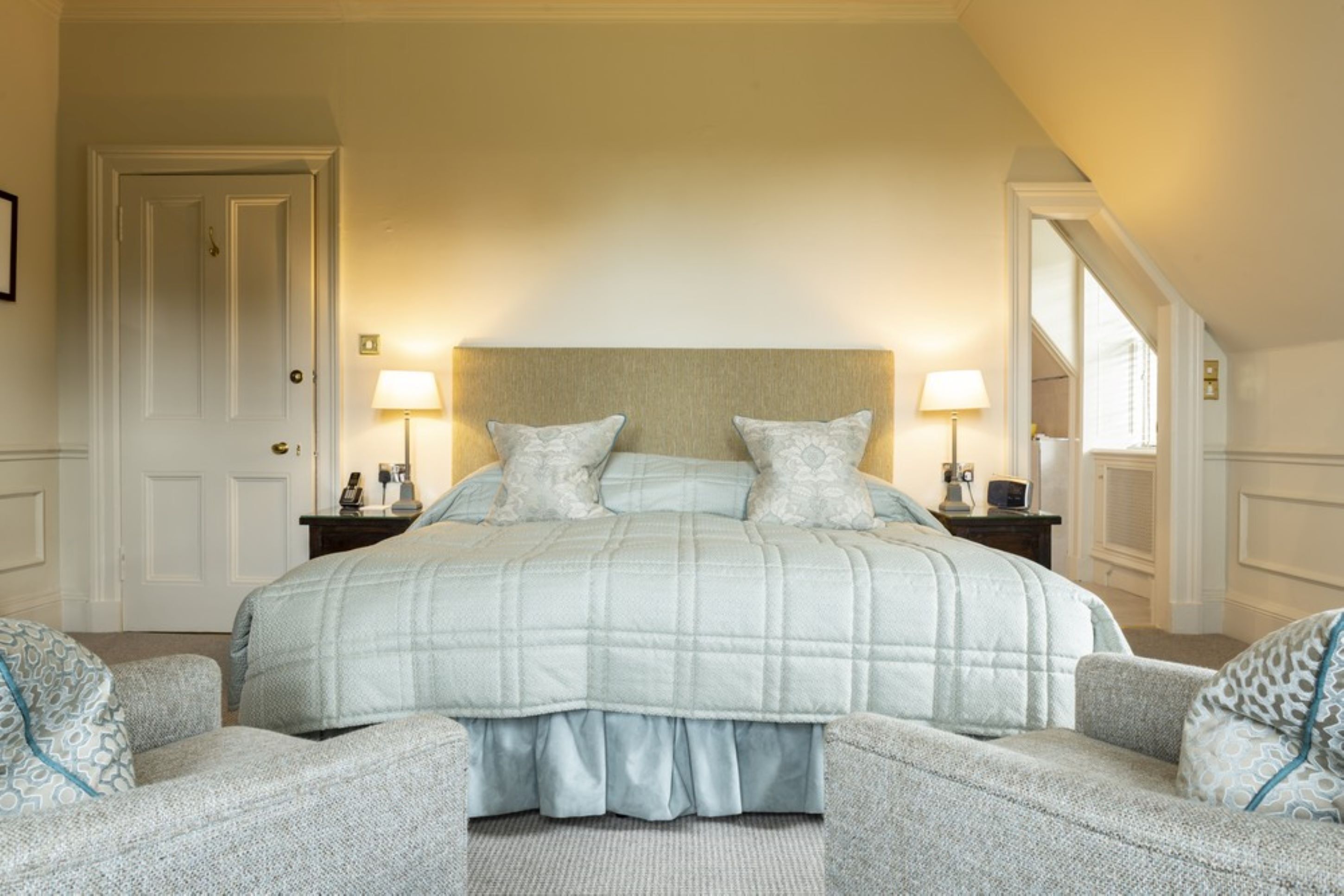 A bedroom with a large bed, two bedside tables with lamps, a door, and a window.