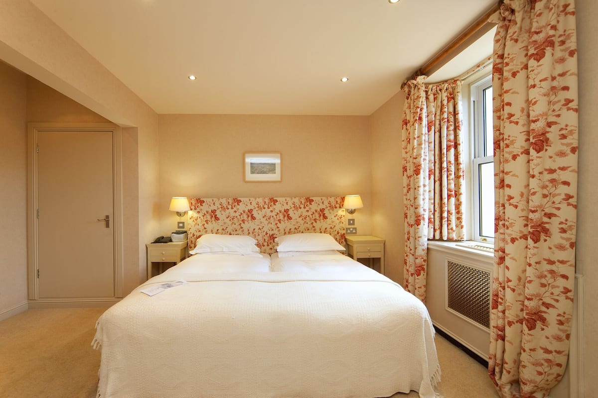 A hotel room with a large bed, two bedside tables with lamps, a window with floral curtains, and a picture on the wall.