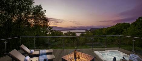A deck with lounge chairs, a hot tub, and a table with a bottle and glasses.