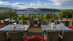 An outdoor dining area with wicker furniture and tables set for a meal, overlooking a lake and mountains. - Isle of Eriska Hotel and Spa (Oban)
