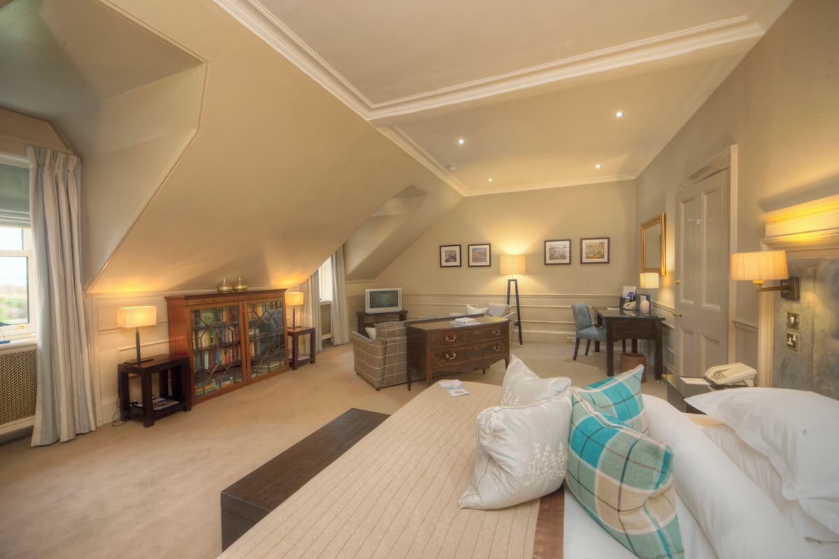 A bedroom with a large bed, a desk, a television, and a wardrobe.