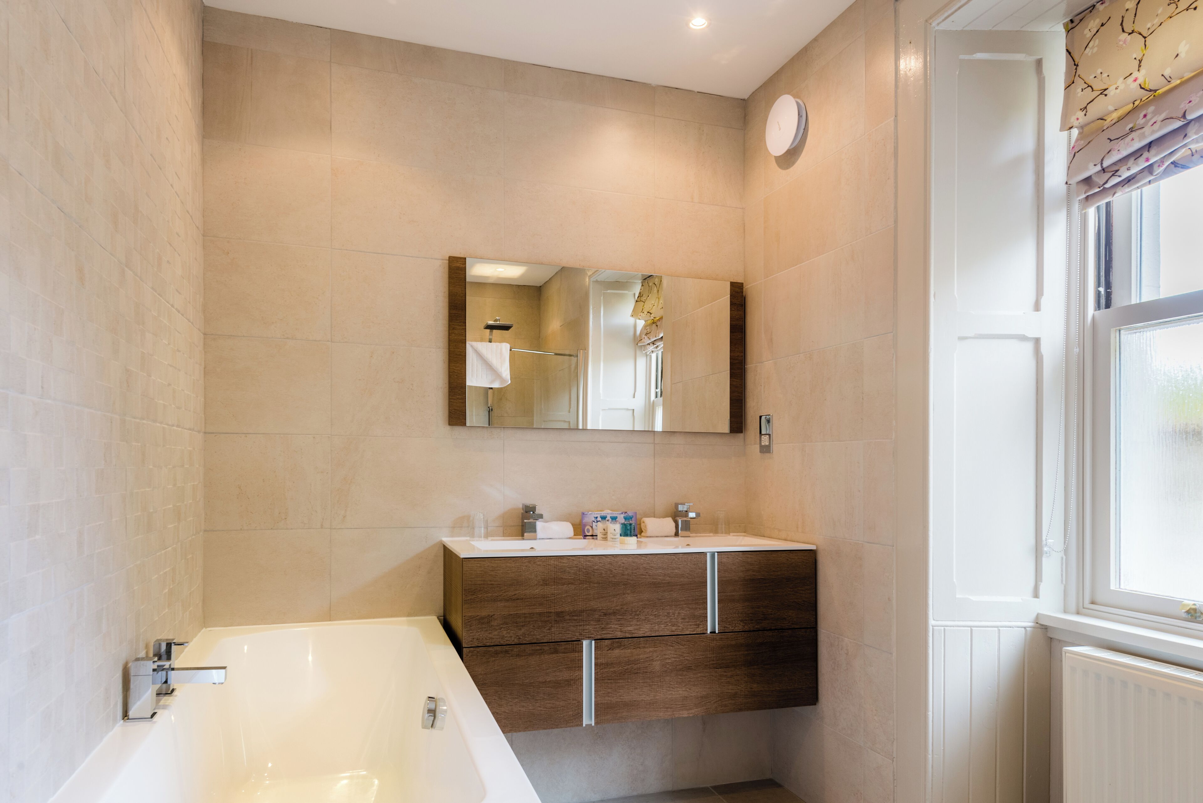 A modern bathroom with a large bathtub, a wooden vanity, and a mirror above the sink.
