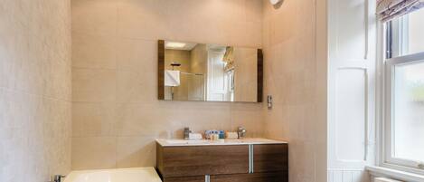A modern bathroom with a large bathtub, a wooden vanity, and a mirror above the sink.