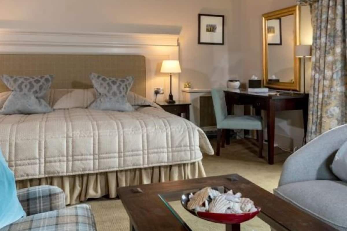 A hotel room with a large bed, a desk, a chair, and a sofa.