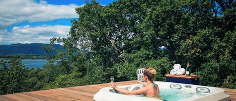 A hot tub on a wooden deck with a scenic view of a lake and mountains.