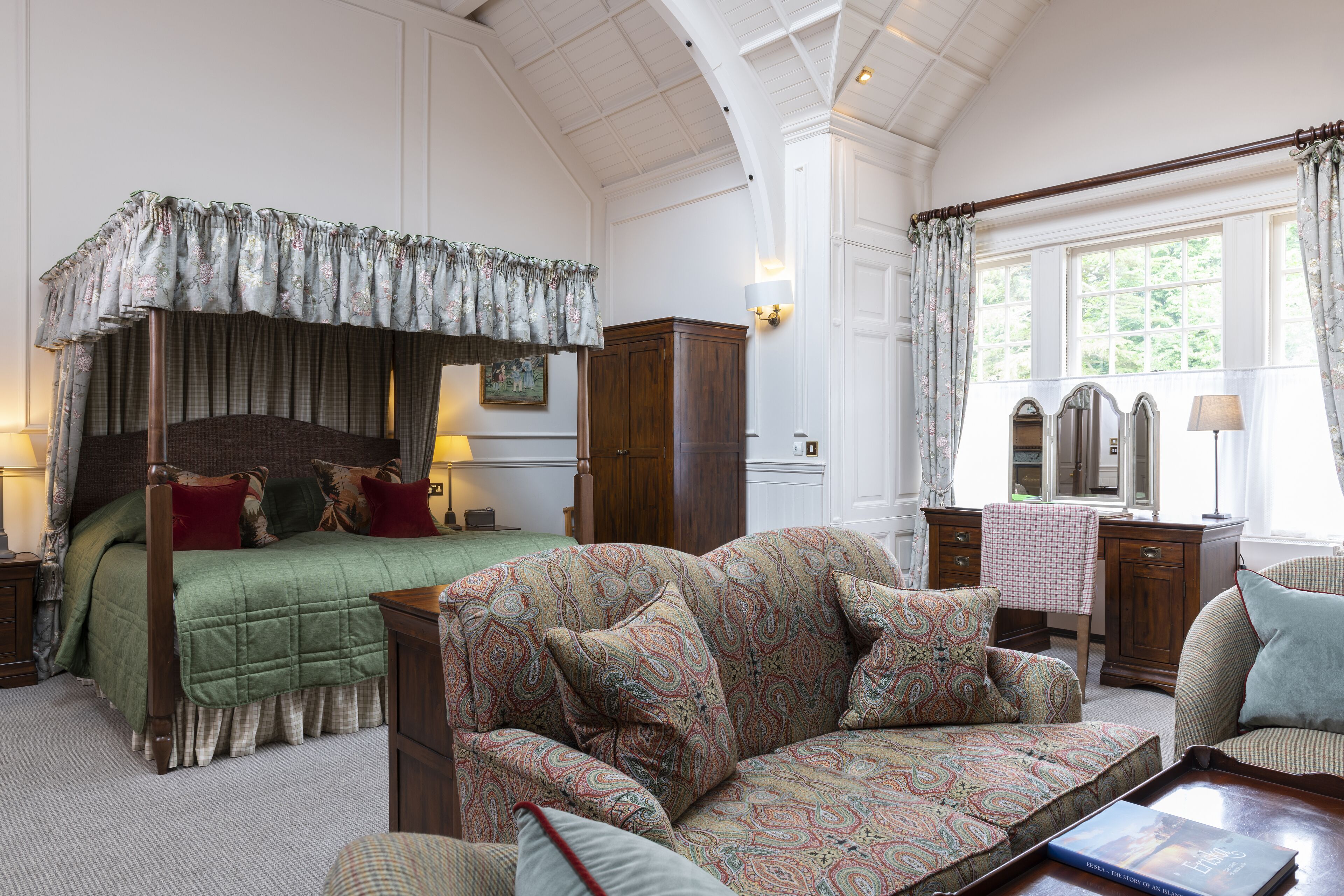 Een slaapkamer met een hemelbed, een bank, een bureau en een stoel.