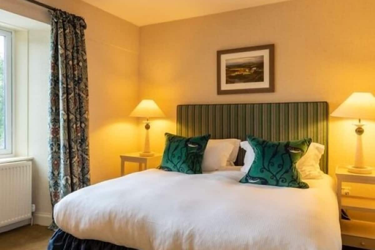 A hotel room with a large bed, two bedside lamps, a framed picture on the wall, and a window with curtains.