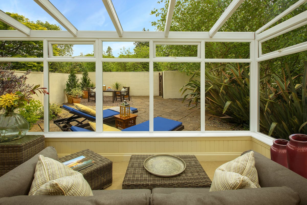 A conservatory with a view of a patio area, including a table, chairs, and a sun lounger.