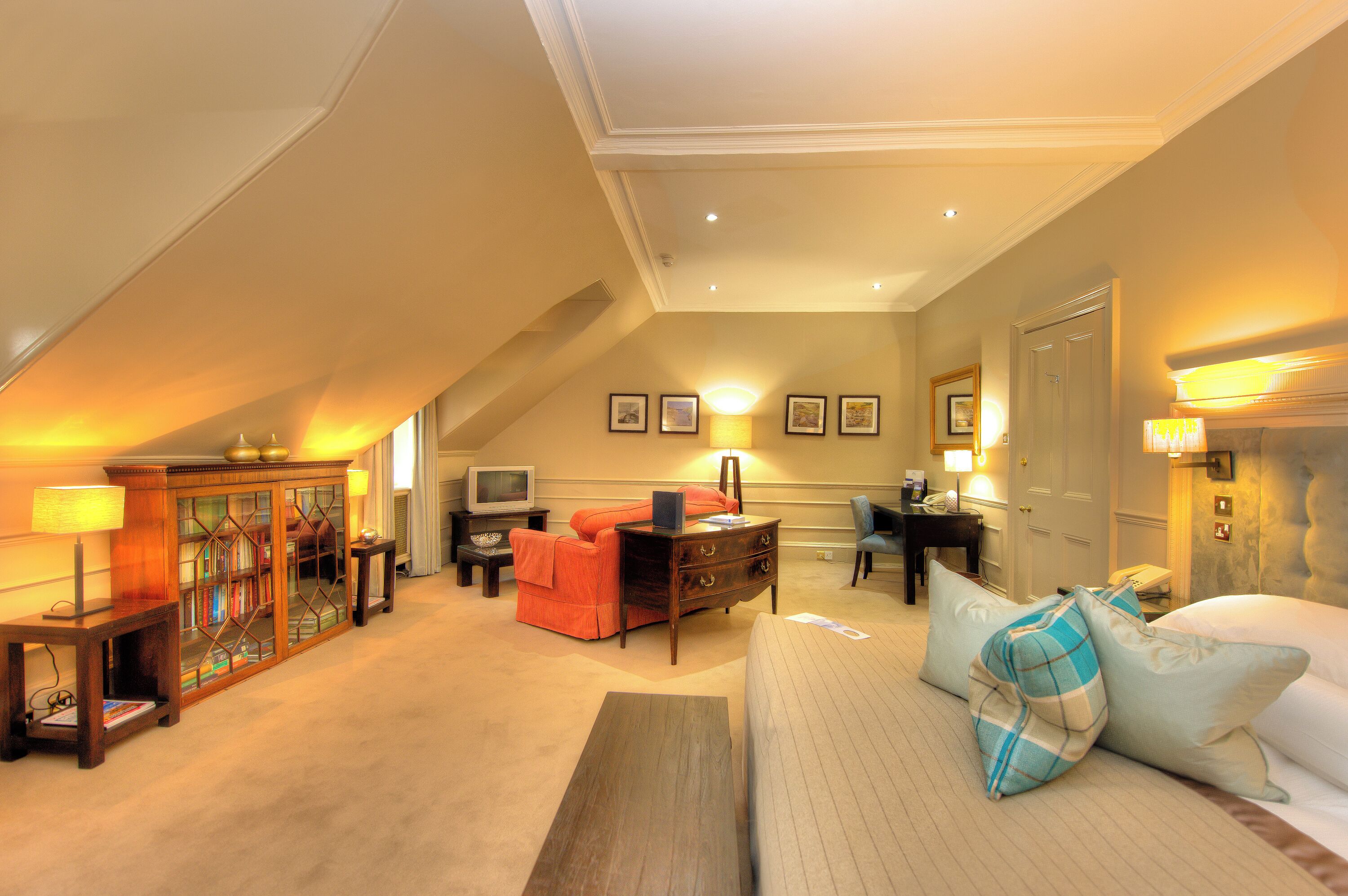 Habitación de hotel con cama, sofá, escritorio con silla, televisor y mueble con libros.
