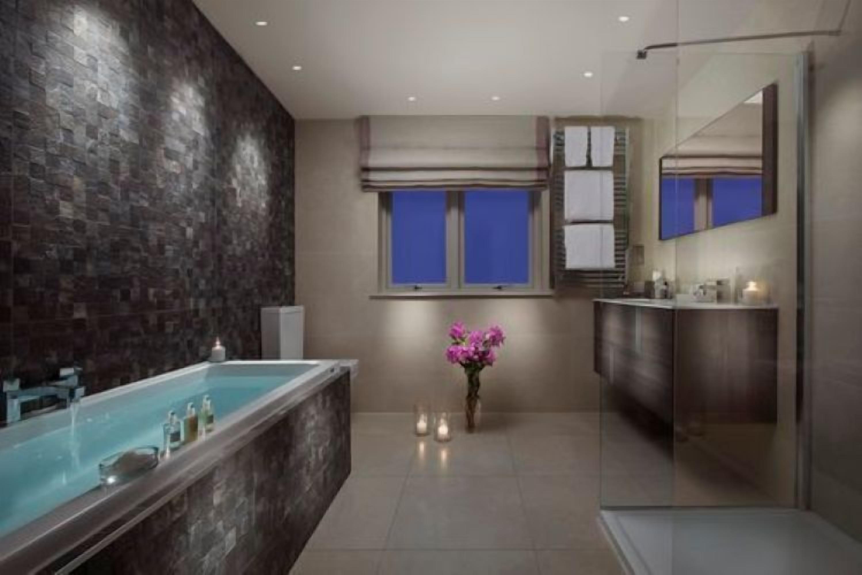 A modern bathroom with a large bathtub, a mirror, and a vase with flowers.