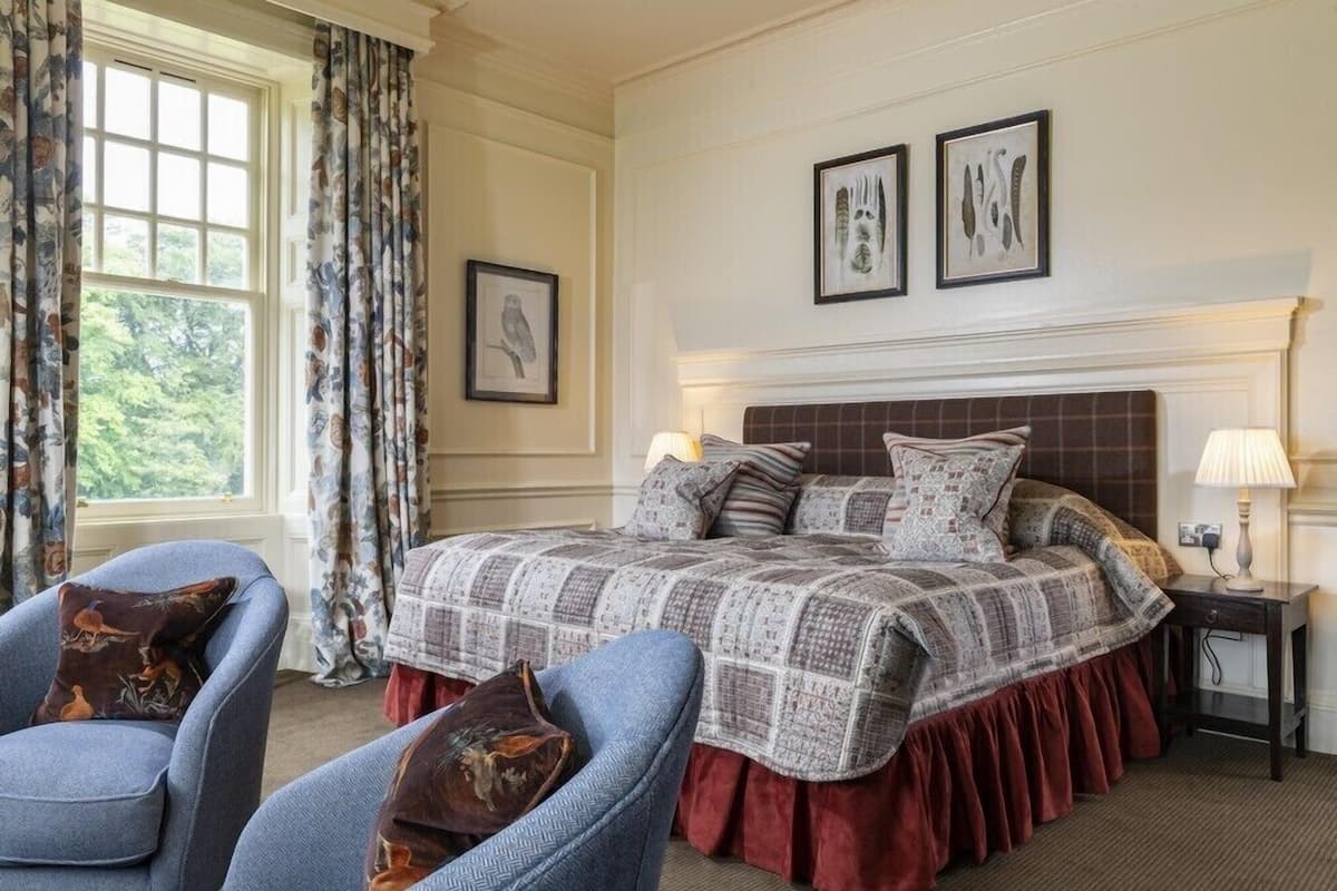 A bedroom with a large bed, two chairs, a nightstand, and a window with curtains.