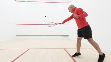 A squash court with a player in a red shirt and black shorts.