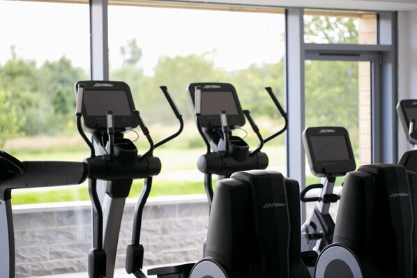 Three stationary bikes with digital screens, positioned in a row with a view of greenery outside.