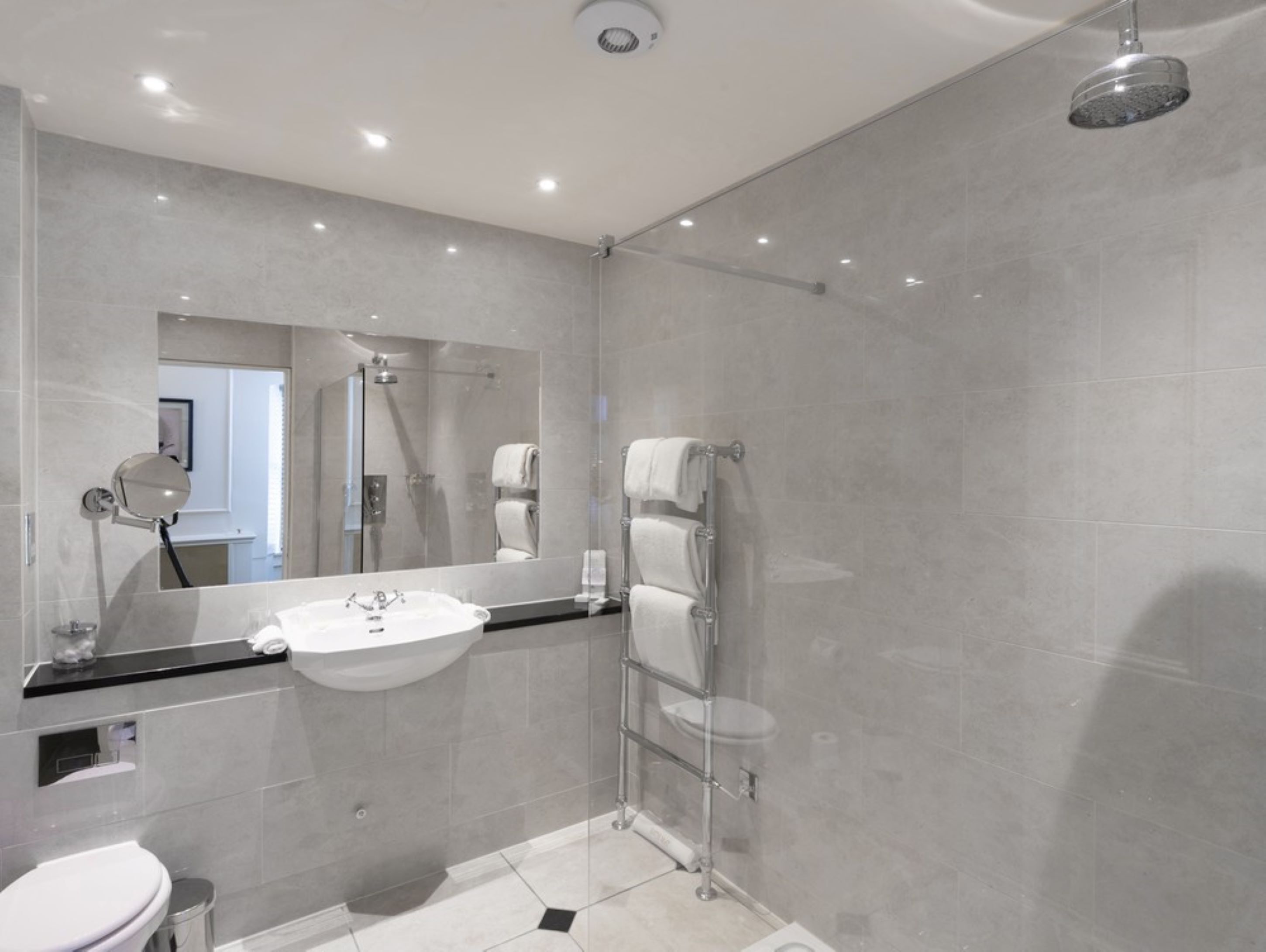 A modern bathroom with a large mirror, a sink, a toilet, and a shower area.