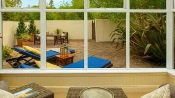 A conservatory with a view of a patio area featuring outdoor furniture, a table, and potted plants.