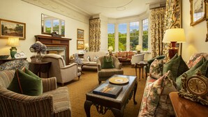 A traditional living room with a fireplace, multiple seating options, and large windows offering a view of greenery. - Isle of Eriska Hotel and Spa (Oban)