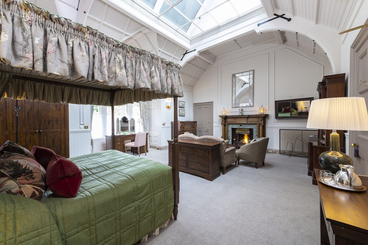 A spacious bedroom with a large bed, a wooden dresser, a fireplace, and a skylight.