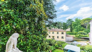 A stone lion statue in a lush garden with a view of a yellow building and a water feature. - Relais & Chateaux Villa Abbazia (Follina)