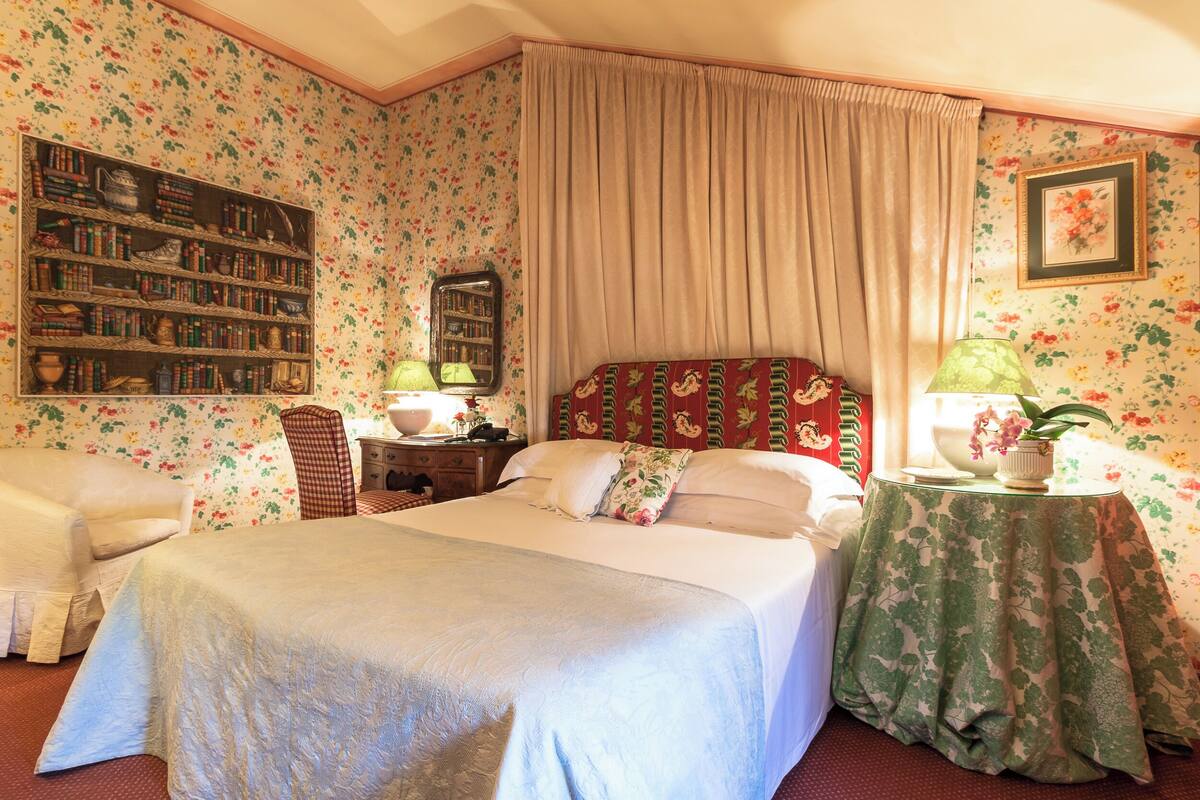 A bedroom with a large bed, a bookshelf, a desk, and a chair.