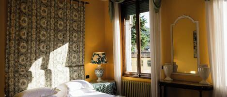 A hotel room with a bed, a table with a lamp, a mirror, and a window with curtains.