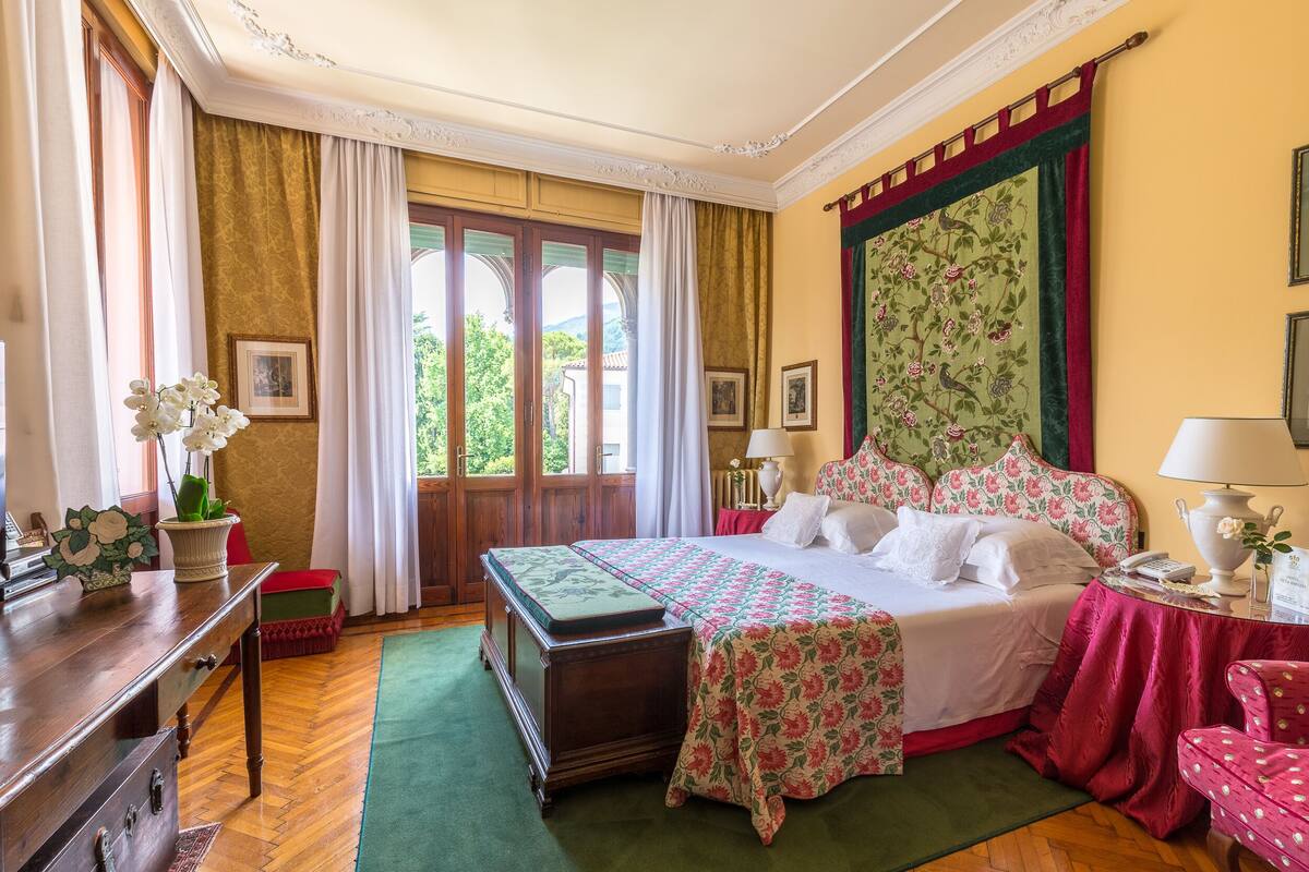 A traditional bedroom with a large bed, a wooden dresser, a desk, and a chair.