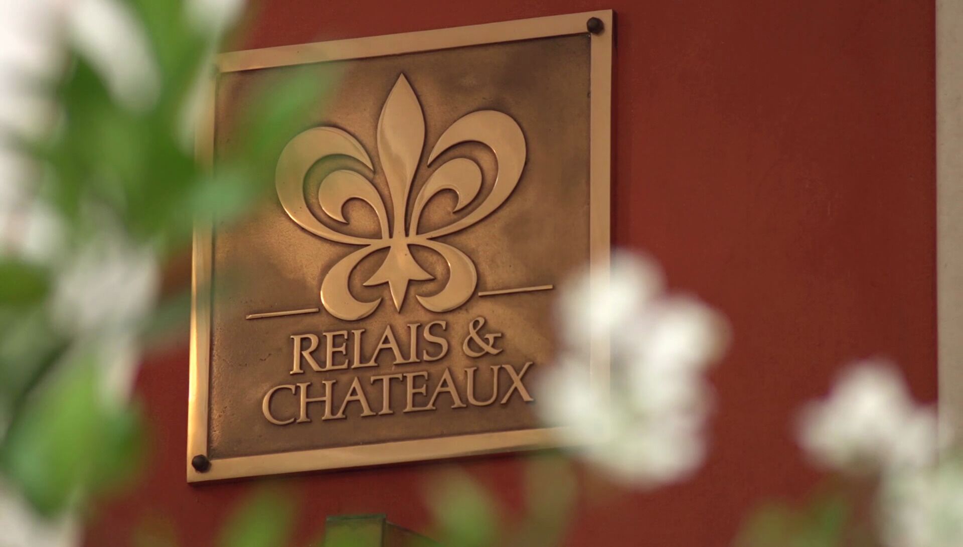 A sign with a fleur-de-lis symbol and the words "RELAIS & CHATEAUX" on a wall.