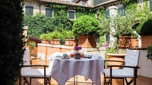 An outdoor patio with a table set for two, surrounded by chairs, with a view of a building and greenery. - Relais & Chateaux Villa Abbazia (Follina)