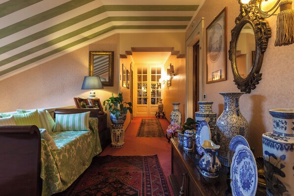 A cozy room with a sloped ceiling, a bed with green bedding, a wooden dresser with blue and white porcelain, and a hallway leading to a door.