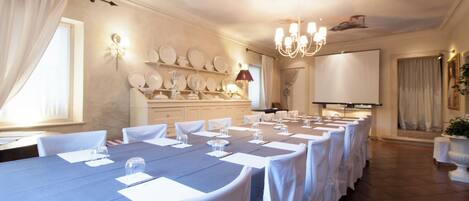 A conference room with a long table, white chairs, a projector screen, and a chandelier.