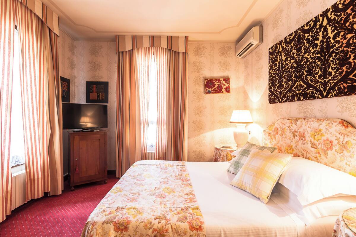 A hotel room with a bed, a television, a nightstand, and a wall-mounted air conditioner.