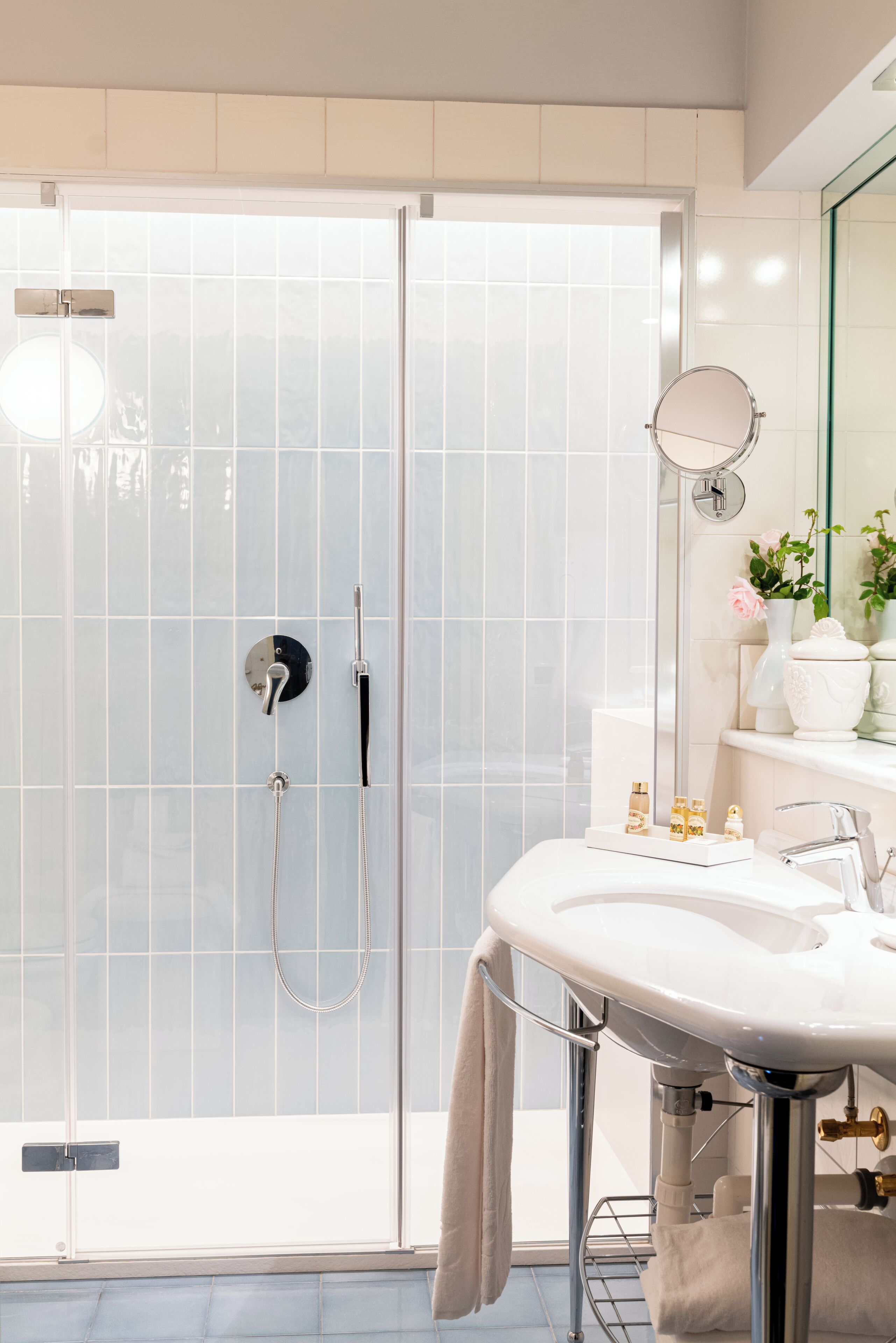 A modern bathroom with a glass-enclosed shower, a white sink with chrome fixtures, and a mirror with a round frame.